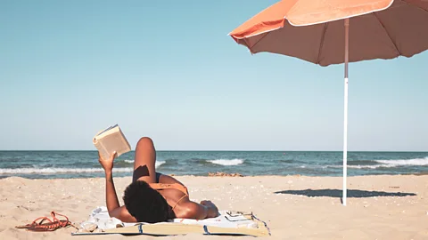 A woman lying on the beach reading a book (Credit: Getty Images)