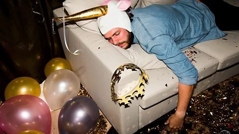 Getty Images A man sleeping on a sofa, surrounded by the debris from a night of partying  (Credit: Getty Images)