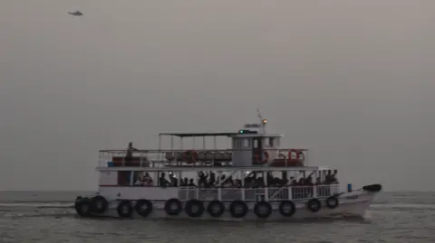 A military helicopter flies over a ferry during a rescue operation after a passenger boat capsized off the coast of Mumbai, India, on 18 December 2024