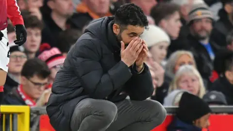 A crouching Ruben Amorim appears to look anguished on the touchline at Manchester United