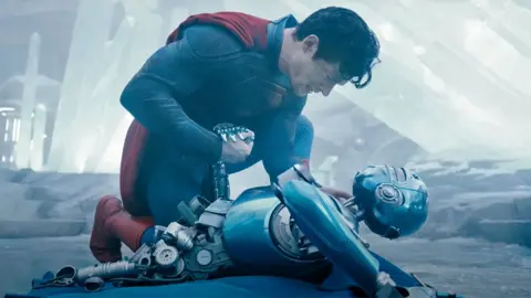 Superman holds the hand of a fallen humanoid robot in a still from the trailer