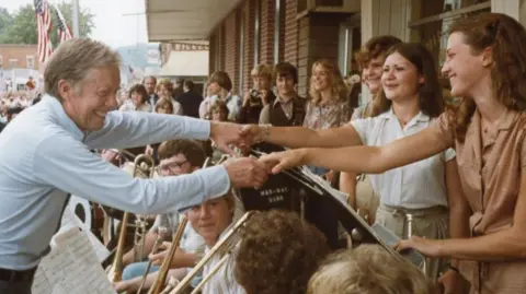 Jimmy Carter smiles and shakes hands with two female supporters in Prairie du Chien, Wisconsin in 1979