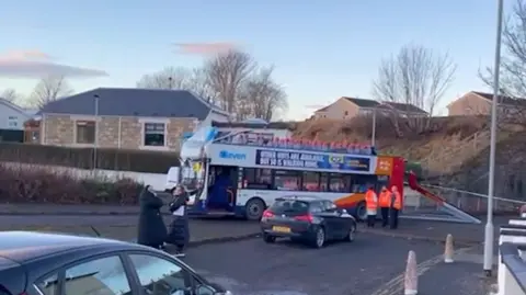 Street scene with double decker bus with its roof torn off.