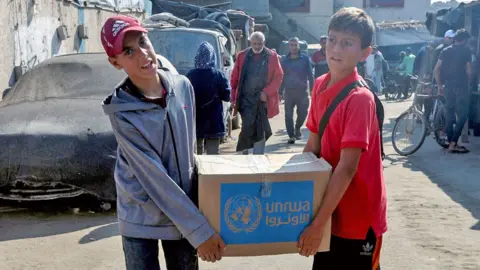 Palestinians carry an aid box distributed by the United Nations Relief and Works Agency amid the Israel-Hamas conflict, in Deir Al-Balah, central Gaza Strip, on 4 November 2024