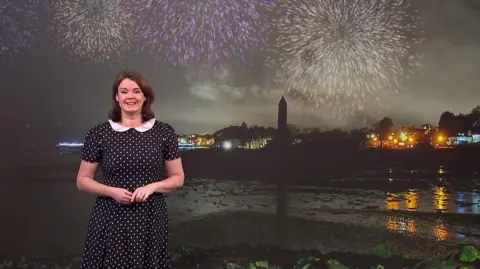 Gillian Smart in a black and white polka dot dress standing in front of an image of the Edinburgh skyline with fireworks overhead.