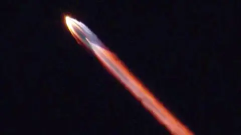 A multicoloured stream of light emanates from a rocket in the night sky.