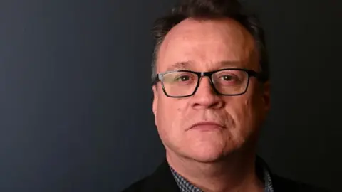 Doctor Who showrunner Russell T Davies wears spectacles against a dark background