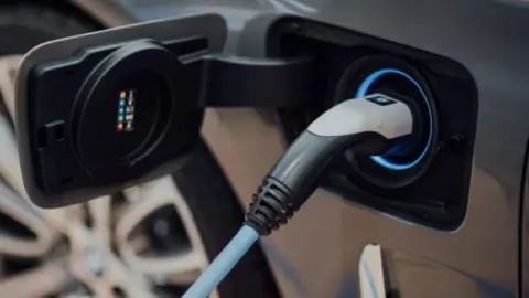 An electric vehicle charger in a car. The lead in blue and the car is a dark grey or black