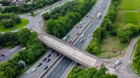 A drone image of a bridge over the M4 motorway. Cars are driving underneath the bridge which is undergoing repair work