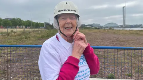 Gladys Speedie wearing a helmet and smiling as she prepares to take a swing