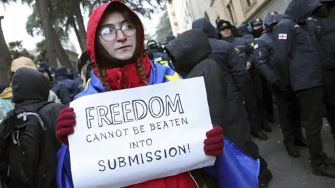 A woman at a protest outside Georgia's parliament in Tbilisi wearing an EU flag and holding a sign that reads "freedom cannot be beaten into submission".