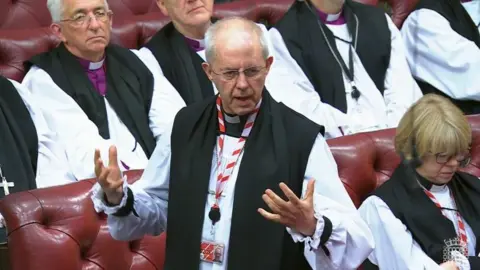 Justin Welby delivers a speech with his hands splayed against a backdrop of the red benches in the House of Lords