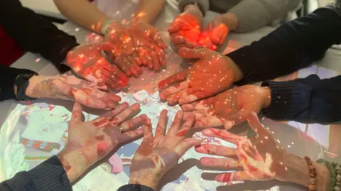 Mark Norman Residents of a care home hold out the palms of their hands in a circle while interacting with light technology