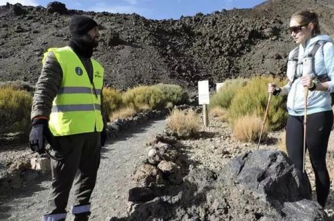 Un agente medioambiental informa a una turista sobre la entrada en vigor de la nueva normativa sobre el acceso a pie al pico del Teide.