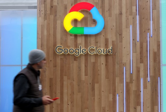 A pedestrian uses a mobile phone as he passes a Google Cloud logo.