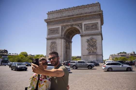 Tourists take selfie pictures in front of the Arc de Triomphe in Paris.