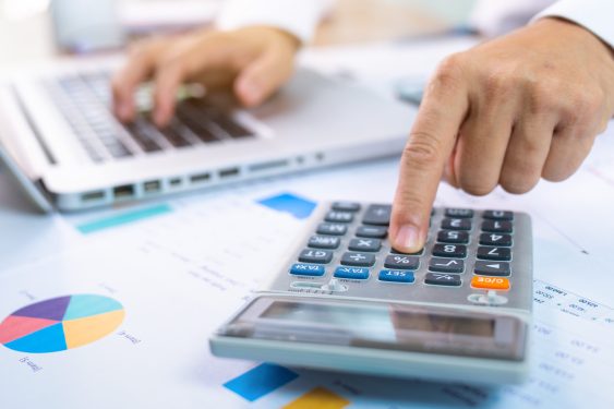 person with one hand typing on a laptop and the other working a calculator