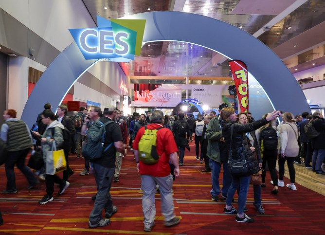 Attendees walk under and pose in front of a CES sign during CES 2024 at the Las Vegas Convention Center.