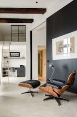 This open-concept Amsterdam loft features soaring 15-foot ceilings, an Eames lounge chair and ottoman, and a Jielde light. Throughout the home, Standard Studio architects Wouter Slot and Jurjen van Hulzen favored raw materials, including concrete, oiled oak, and hot-rolled steel, all of which complemented the original space's industrial feel. Tucked smartly underneath the loft, a compact home office features functional built-in shelving and an Eames DSR chair.