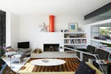 A home near Rye, England, opens onto a deck through a Sunflex door. The living room features a sofa by Terence Woodgate, 620 chairs by Dieter Rams for Vitsœ, and an Oluce Atollo 239 lamp by Vico Magistretti. The wood-burning fireplace sits along one wall in the room, with a bright orange flue acting as a sculptural focal point.