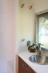 The bathroom has a stainless-steel sink and faucet, Hanex solid surface countertops, and Schoolhouse Electric pulls.