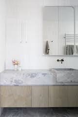 Limestone floor tiles sync with a vanity counter formed in Elba Dolomite, complete with integrated sinks of the same material. Thassos Marble Kit Kat Tiles cover the wall. The mirror is a Robson Rak-designed mirror cabinet painted in Dulux Natural White.