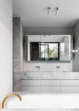 Light gray mosaic wall tile meets a pronounced slab of Natural Jeremiel Grey Marble in the vanity. The tile grid is softened by Waterstone polished plaster. The wall-mounted, brass faucets are by Vola.