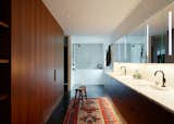 The focal point is a deep soaking tub clad in marble. Abundant walnut cabinetry and a marble counter adhere to the predominant material palette. The flooring is stained oak. 