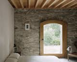 A bedroom on the ground level juxtaposes the saved stonework with an exposed wood ceiling and lime plaster walls.