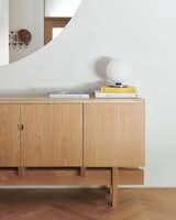 A detailed shot of one of the custom storage pieces designed by Berg, a sideboard against the dining room wall under the circular interior window. The floors throughout are the main source of pattern in the minimalist palette, and they are white oak laid in a herringbone arrangement.