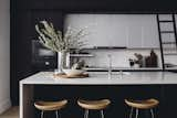 Contrast continues in the kitchen with a black-and-white palette warmed by natural wood elements. A Caesarstone countertop and backsplash with alabaster cabinets add a bright pop to the otherwise inky space—even the Miele and SubZero appliances are in dark tones. Arranged throughout are an Etu Home pizza board, Terrain ceramic fruit bowl, Waterworks cannisters, West Elm mortar and pestle, and a House Dr. utensil pot. 