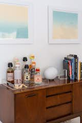 A Gregg Table Lamp by Foscarini sits atop a vintage credenza that the couple use as a bar. The gradient landscape diptych prints above are by Erin.