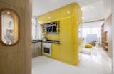 The centrally located kitchen volume is faced with high-gloss lacquered panels and features a yellow tile backsplash with black artificial stone countertops.

