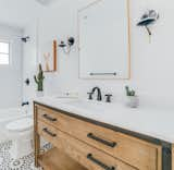 The new hall bathroom features Agdal Black cement floor tiles from Moroccan Mosaics, a vanity by Sage Hill Designs with a white quartz countertop by Stone Design by Santos, and a CB2 mirror.