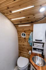 The bathroom is outfitted with a Nature's Head composting toilet, stainless steel sink, and custom cabinets. The countertop and curved wall are built from cedar. The LED lighting strips add a modern touch.