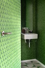 A 1930s terrace house in London saw a transformation by Gruff Architects, complete with a new powder room whose green leaf wallpapered interiors flow onto the back of the bathroom door. White and green tiles at the floor provide a contrast of scale while still maintaining the color scheme.