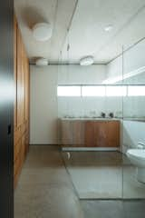 The main bathroom features warmly crafted timber joinery contrasted with terrazzo-style concrete floors and industrial concrete ceilings.