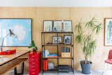 The neutral backdrop of plywood and dove grey carpet is contrasted with bright red feature furniture pieces and potted plants.