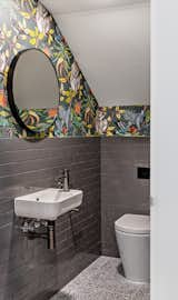 An under-the-stairs powder room is transformed into an exciting space in this home in Australia, where the gray subway tile gives way to a colorful printed wallpaper.