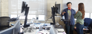 Image of two coworkers meeting next to a computer in their office.