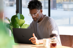 Picture of a man seated at a table, looking down at a computer.