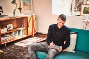 A man sitting on a couch writing in a notebook