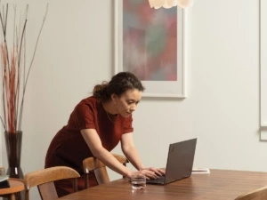 A woman at her diningroom table looking at a Lenovo ThinkPad Yoga. Remote Working collection. Keywords: remote work, remote working, work from home, working at home, home office