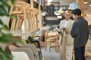 Retail store manager working with a customer, showing merchandise and providing customer service on-the-go using a tablet to locate inventory and place orders. Keywords: Two people; transaction; furniture; in store pick up; point of sale; POS; point-of-sale; small business; Dynamics 365; modern commerce experiences; secure purchase