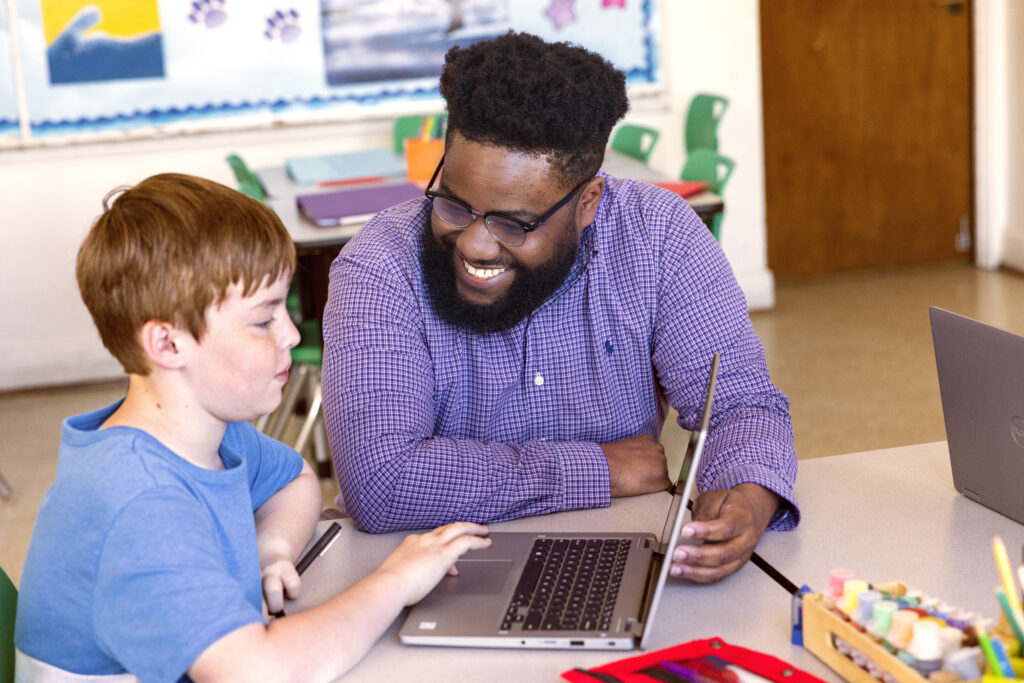 A teacher working with a student on a laptop in a classroom setting, using Microsoft Copilot. 