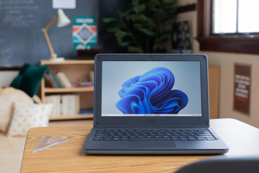 An open laptop with Windows 11 on a desk in an elementary school classroom. 