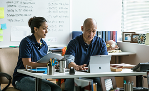 Image of two firstline workers sitting behind a desk making plans on their laptops.