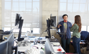 Image of two coworkers meeting next to a computer in their office.