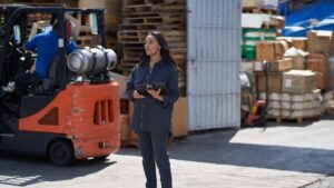 Female manufacturing worker holding tablet device while monitoring work outside of a factory.