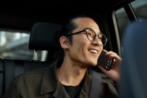 A man talking on his mobile phone, using Teams phone, while sitting in the backseat of a vehicle​.